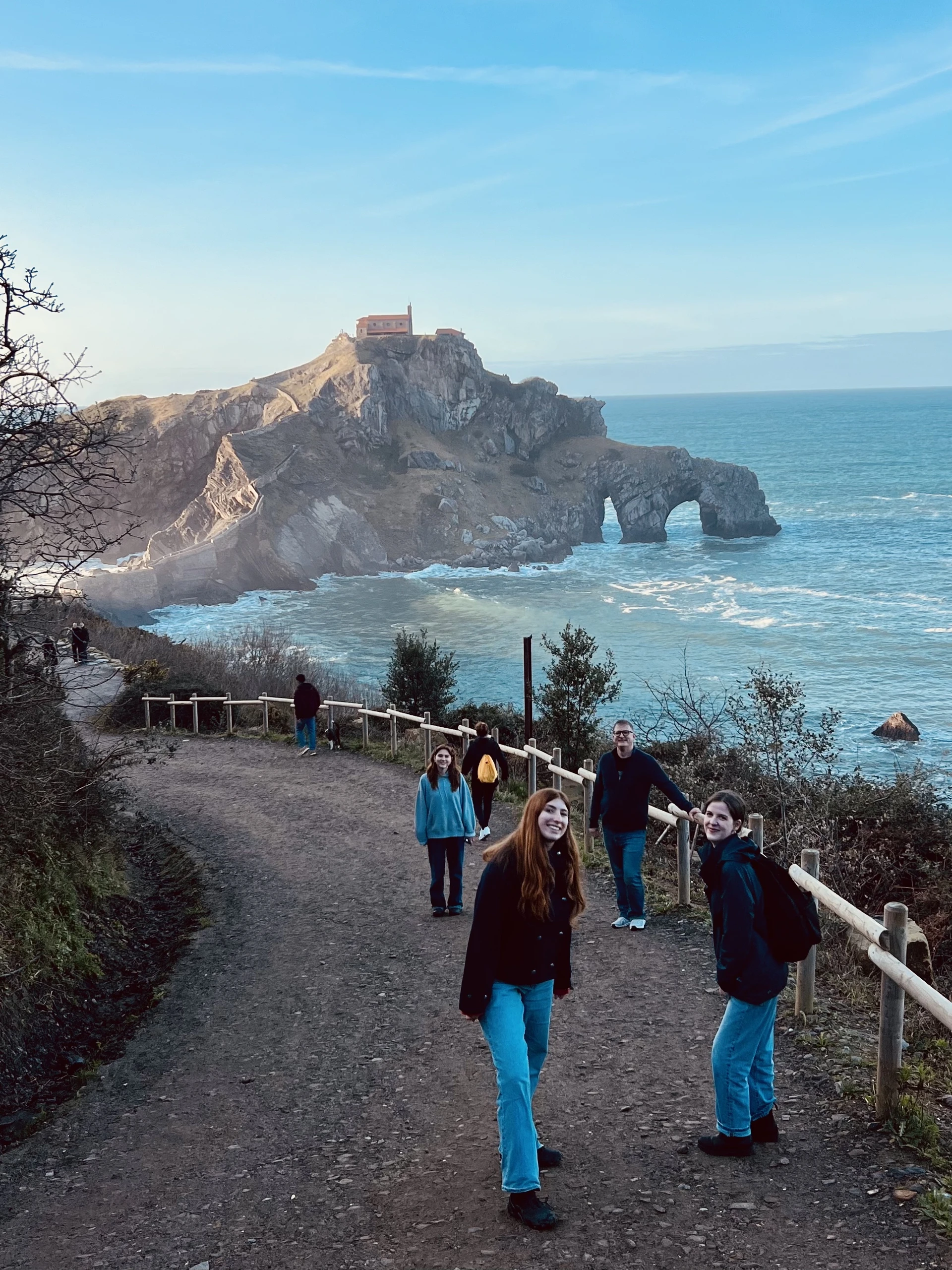 Students stand smiling at the camera along a winding trail to an impressive structure built atop a cliff.